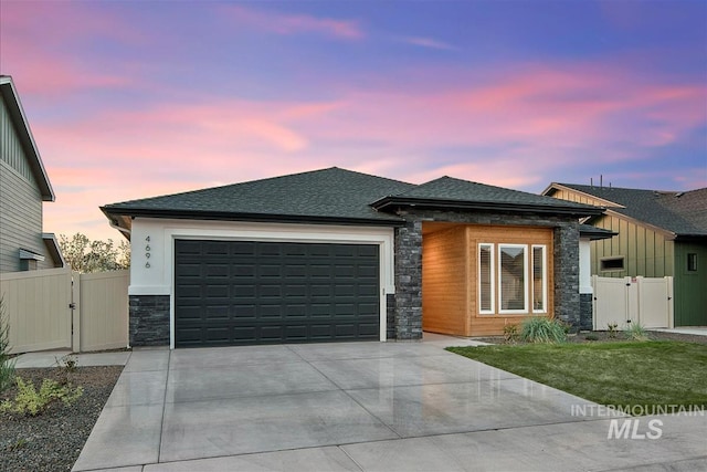 prairie-style home with a gate, stone siding, concrete driveway, and a garage