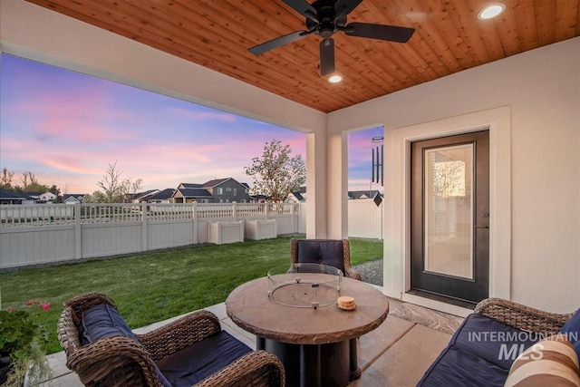 patio terrace at dusk featuring a fenced backyard, ceiling fan, and a lawn
