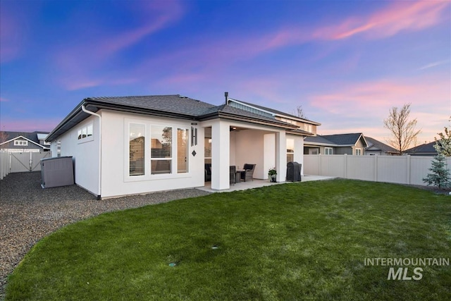 back of house at dusk with a fenced backyard, a yard, a patio, and stucco siding