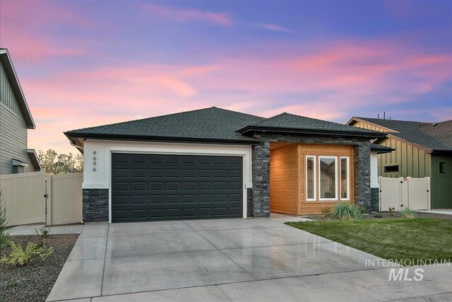 prairie-style home with a gate, stone siding, concrete driveway, and a garage