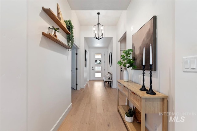 doorway to outside with baseboards, an inviting chandelier, and light wood-type flooring