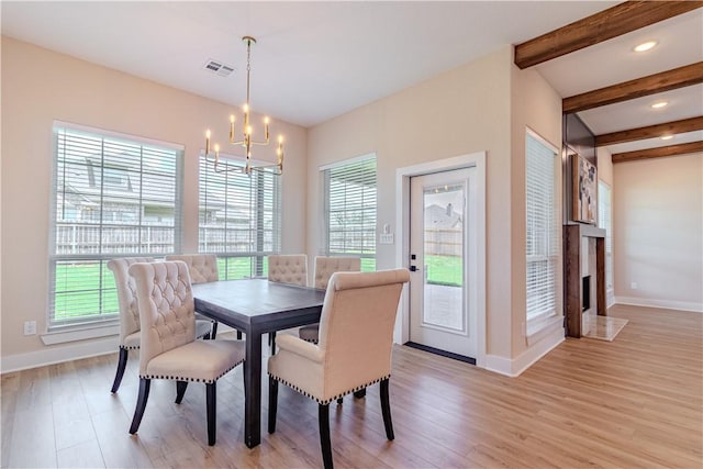 dining space with beamed ceiling, a notable chandelier, a premium fireplace, and light wood-type flooring