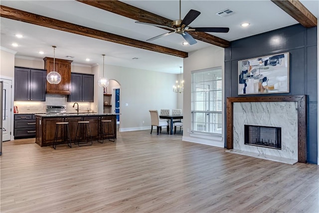 kitchen featuring pendant lighting, a breakfast bar, an island with sink, stone countertops, and light wood-type flooring