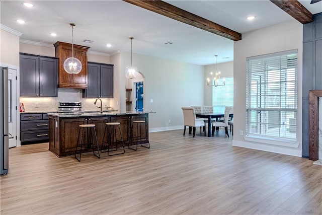 kitchen featuring light hardwood / wood-style flooring, a kitchen island with sink, dark stone countertops, and decorative light fixtures