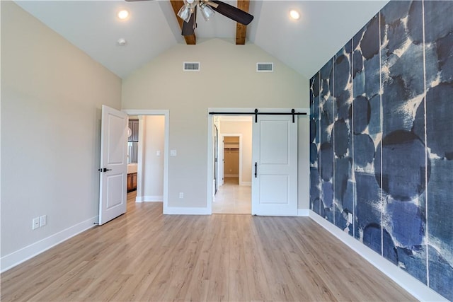 unfurnished bedroom with a barn door, light wood-type flooring, high vaulted ceiling, and beam ceiling