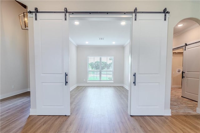 interior space featuring ornamental molding, a barn door, and light hardwood / wood-style floors