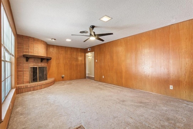 unfurnished living room with carpet flooring, a brick fireplace, ceiling fan, and wooden walls