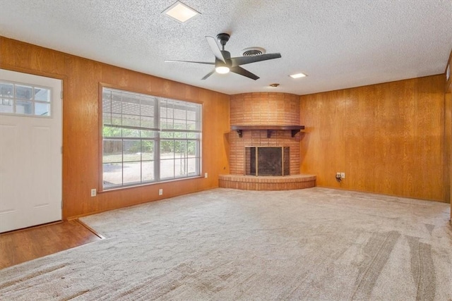 unfurnished living room featuring wood walls, carpet floors, a textured ceiling, and a brick fireplace