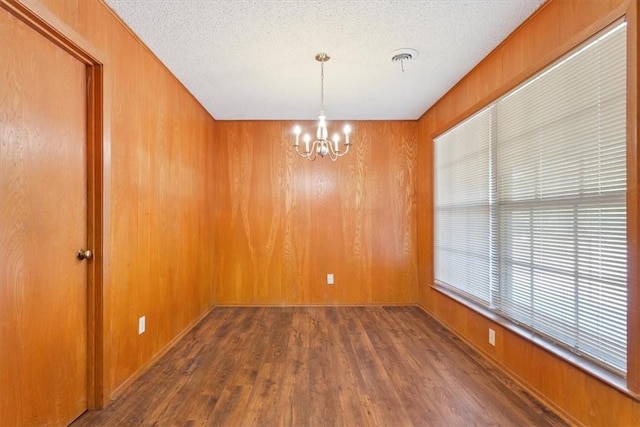 empty room with dark hardwood / wood-style flooring, a textured ceiling, wooden walls, and an inviting chandelier