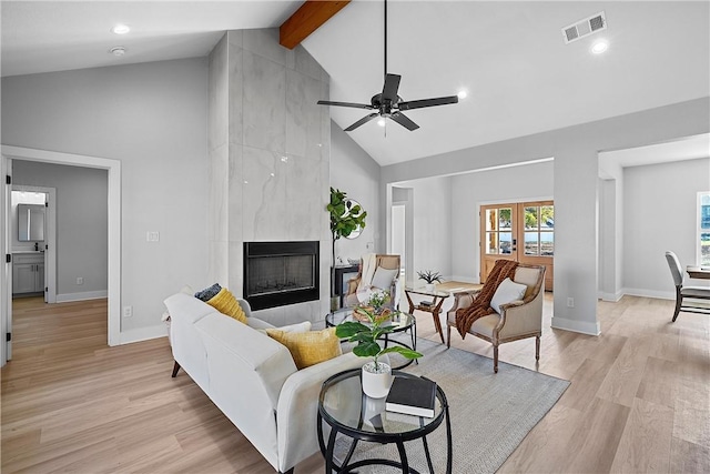 living room with light wood-type flooring, ceiling fan, high vaulted ceiling, a premium fireplace, and beamed ceiling