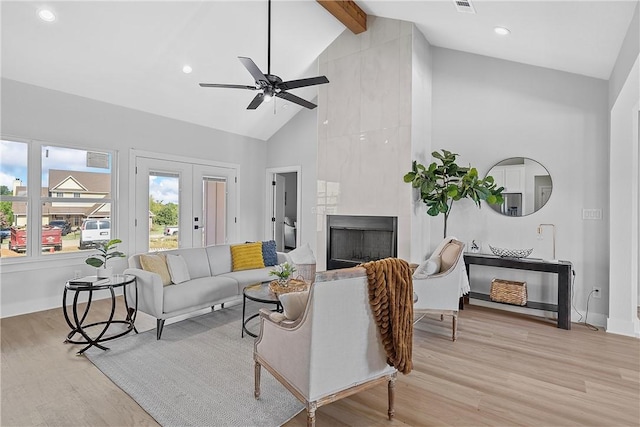 living room featuring light wood-type flooring, a large fireplace, ceiling fan, beam ceiling, and high vaulted ceiling