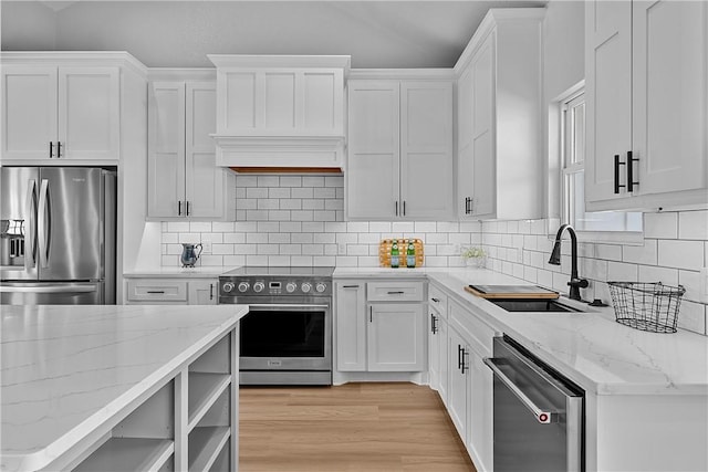 kitchen with white cabinetry, sink, stainless steel appliances, light stone counters, and light hardwood / wood-style floors