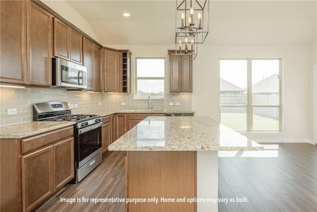 kitchen with stainless steel appliances, light stone counters, pendant lighting, vaulted ceiling, and a kitchen island