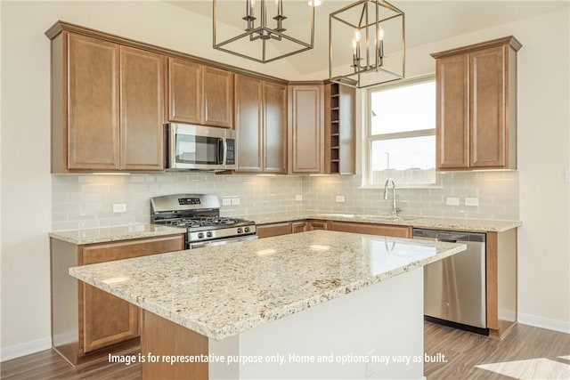 kitchen with appliances with stainless steel finishes, light stone counters, decorative light fixtures, hardwood / wood-style floors, and a center island