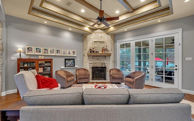 living room with ceiling fan, french doors, a raised ceiling, a stone fireplace, and hardwood / wood-style flooring