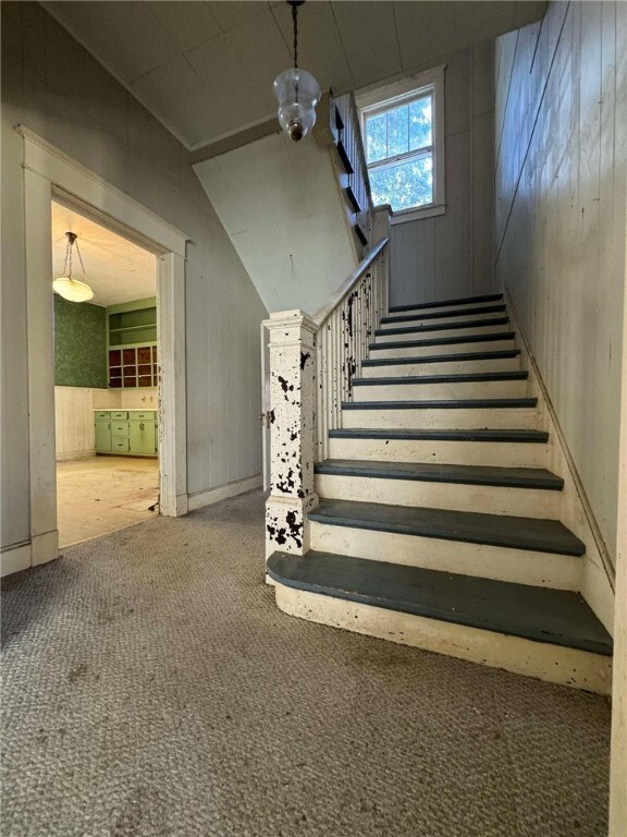 stairway featuring a notable chandelier, carpet floors, and wooden walls