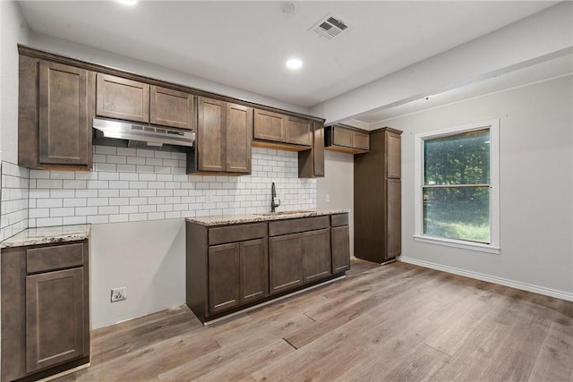 kitchen featuring light wood-type flooring, backsplash, light stone counters, and sink