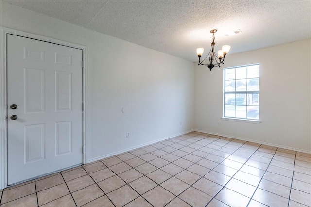 tiled empty room featuring a textured ceiling and an inviting chandelier