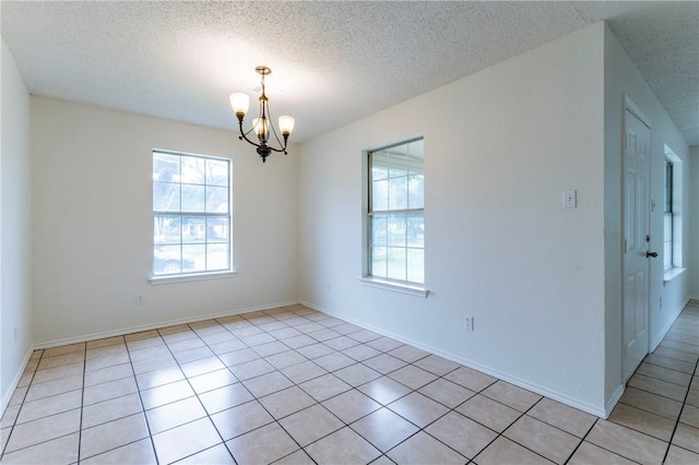 tiled empty room with a textured ceiling and an inviting chandelier