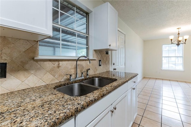 kitchen with white cabinetry, sink, a notable chandelier, dark stone countertops, and decorative backsplash