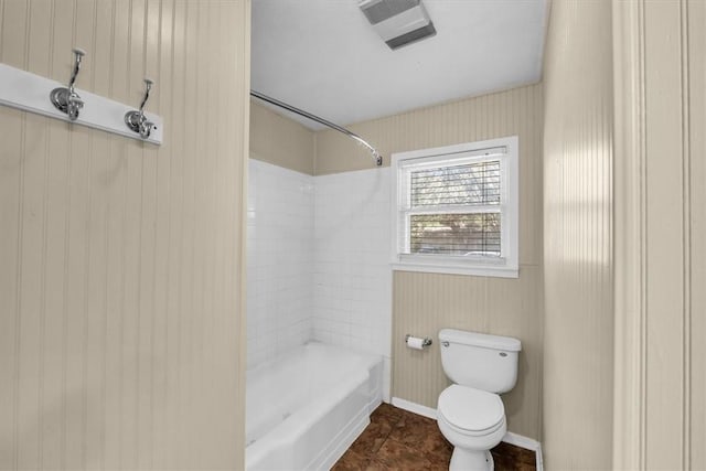 bathroom featuring tile patterned floors, wooden walls, tiled shower / bath, and toilet