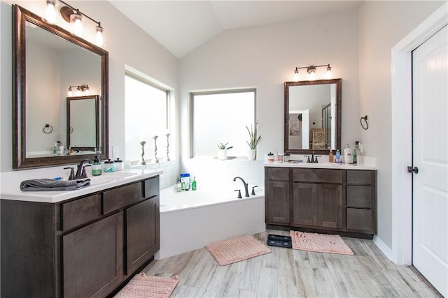 bathroom featuring vanity, hardwood / wood-style floors, vaulted ceiling, and a bath