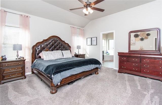 bedroom with ceiling fan, light colored carpet, vaulted ceiling, and ensuite bath