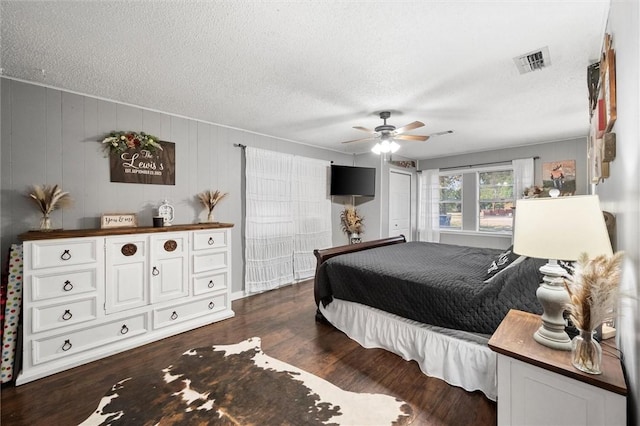 bedroom featuring ceiling fan, dark hardwood / wood-style flooring, a textured ceiling, and wooden walls