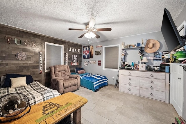 bedroom featuring wood walls, ceiling fan, and a textured ceiling