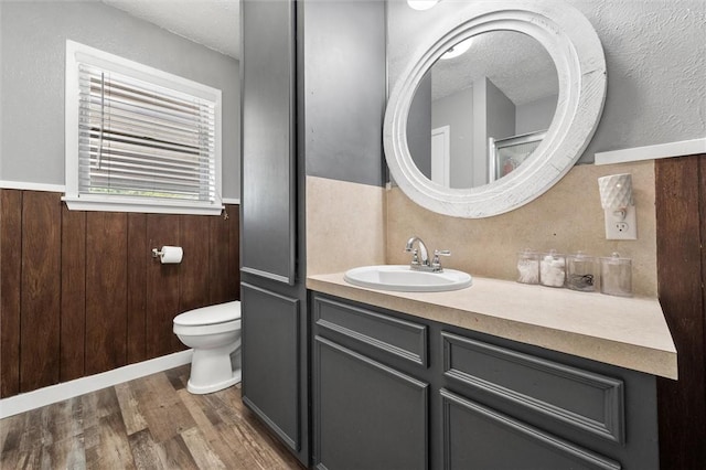 bathroom featuring vanity, a textured ceiling, wood-type flooring, toilet, and wood walls