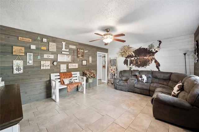 living room with wood walls, ceiling fan, and a textured ceiling