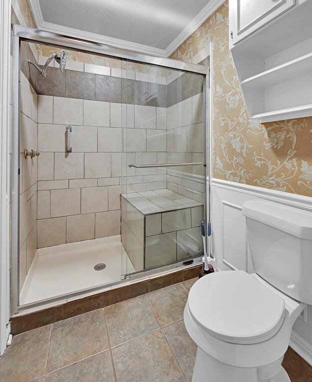 full bathroom featuring toilet, ornamental molding, wallpapered walls, a shower stall, and wainscoting