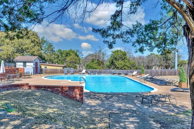 community pool with an outbuilding, a patio area, and fence