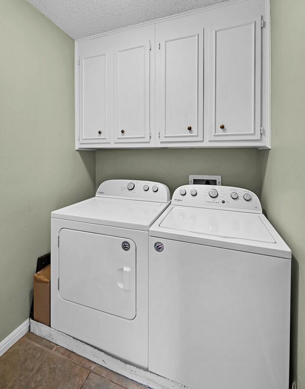 washroom with baseboards, tile patterned floors, cabinet space, a textured ceiling, and independent washer and dryer