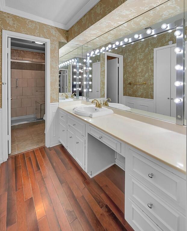 bathroom featuring wallpapered walls, wainscoting, a stall shower, wood finished floors, and vanity