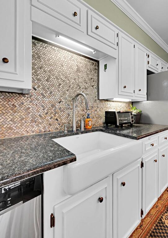 kitchen featuring tasteful backsplash, crown molding, dishwasher, dark stone counters, and white cabinets