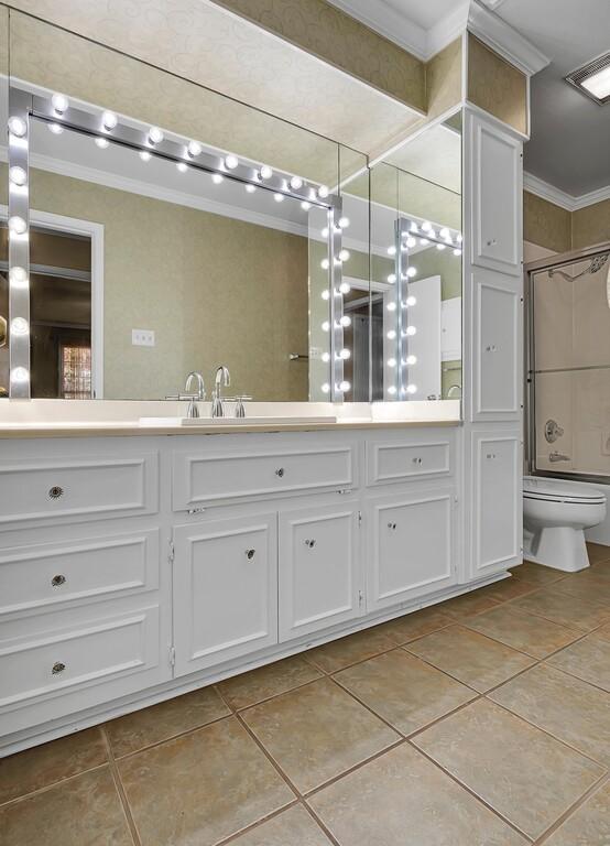 full bathroom with a shower with shower door, toilet, ornamental molding, and vanity