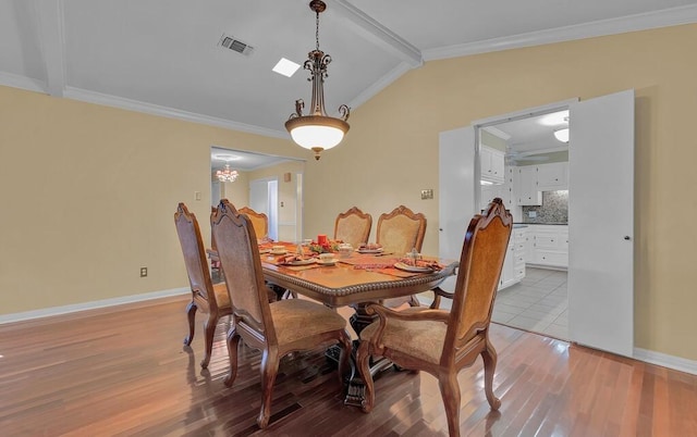 dining room featuring light wood-type flooring, visible vents, lofted ceiling, ornamental molding, and baseboards