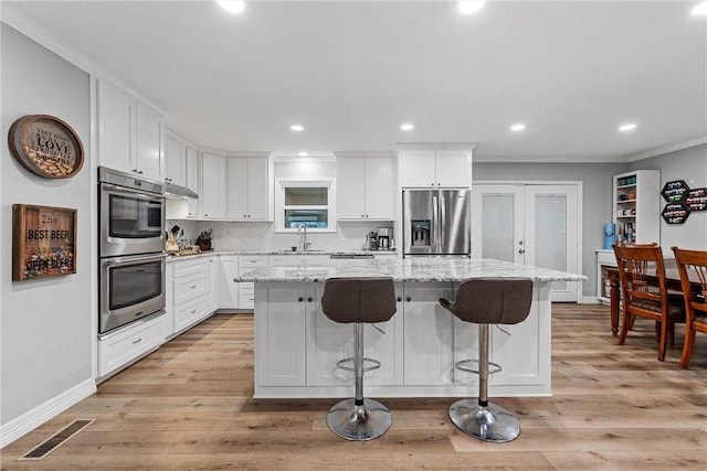 kitchen with stainless steel appliances, a kitchen island, visible vents, white cabinets, and light stone countertops