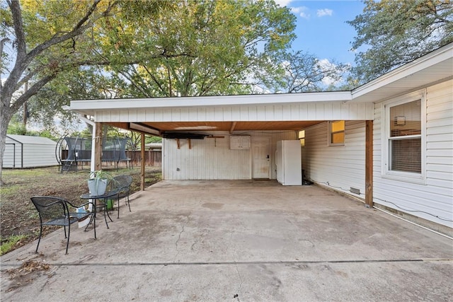 view of patio featuring an attached carport, fence, driveway, a storage unit, and a trampoline