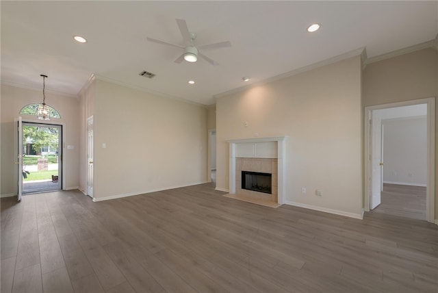 unfurnished living room featuring ceiling fan with notable chandelier, wood-type flooring, crown molding, and a tile fireplace