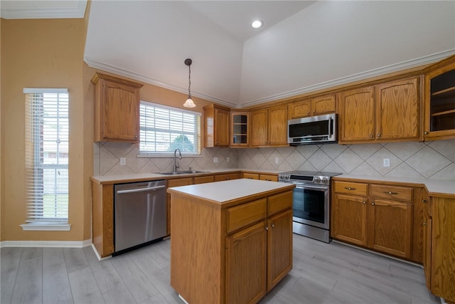 kitchen with sink, appliances with stainless steel finishes, decorative light fixtures, a kitchen island, and light wood-type flooring