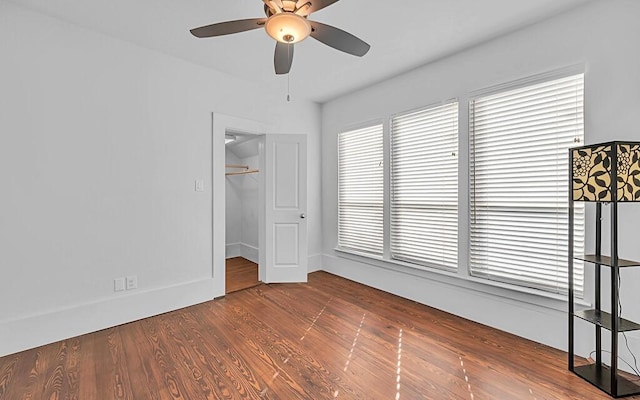 unfurnished bedroom featuring hardwood / wood-style floors, ceiling fan, a walk in closet, and a closet