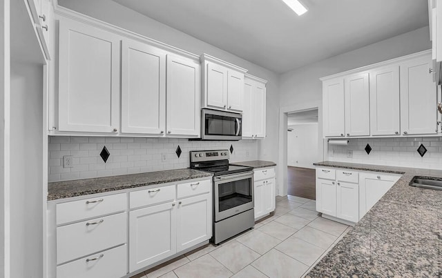 kitchen with appliances with stainless steel finishes, tasteful backsplash, dark stone counters, light tile patterned floors, and white cabinets