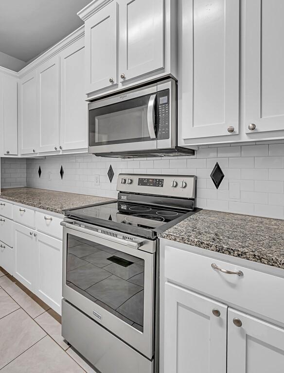 kitchen featuring white cabinetry, light tile patterned flooring, dark stone counters, and appliances with stainless steel finishes