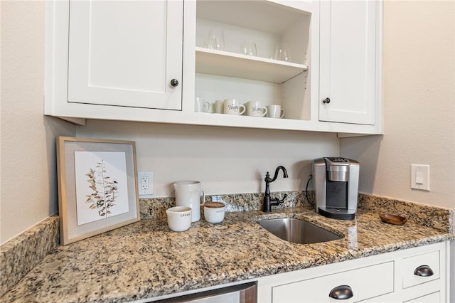 kitchen featuring light stone counters, white cabinetry, and sink