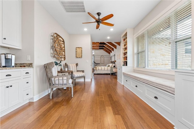 living area with beam ceiling, ceiling fan, and light hardwood / wood-style flooring