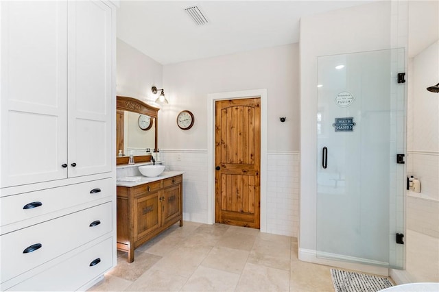 bathroom featuring tile patterned flooring, vanity, a shower with shower door, and tile walls