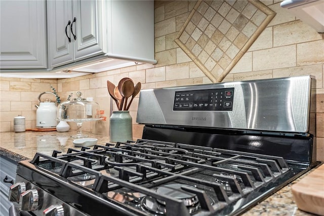 details featuring light stone countertops, backsplash, and stainless steel range with gas stovetop