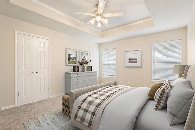 bedroom featuring ceiling fan, light colored carpet, a tray ceiling, a closet, and ornamental molding